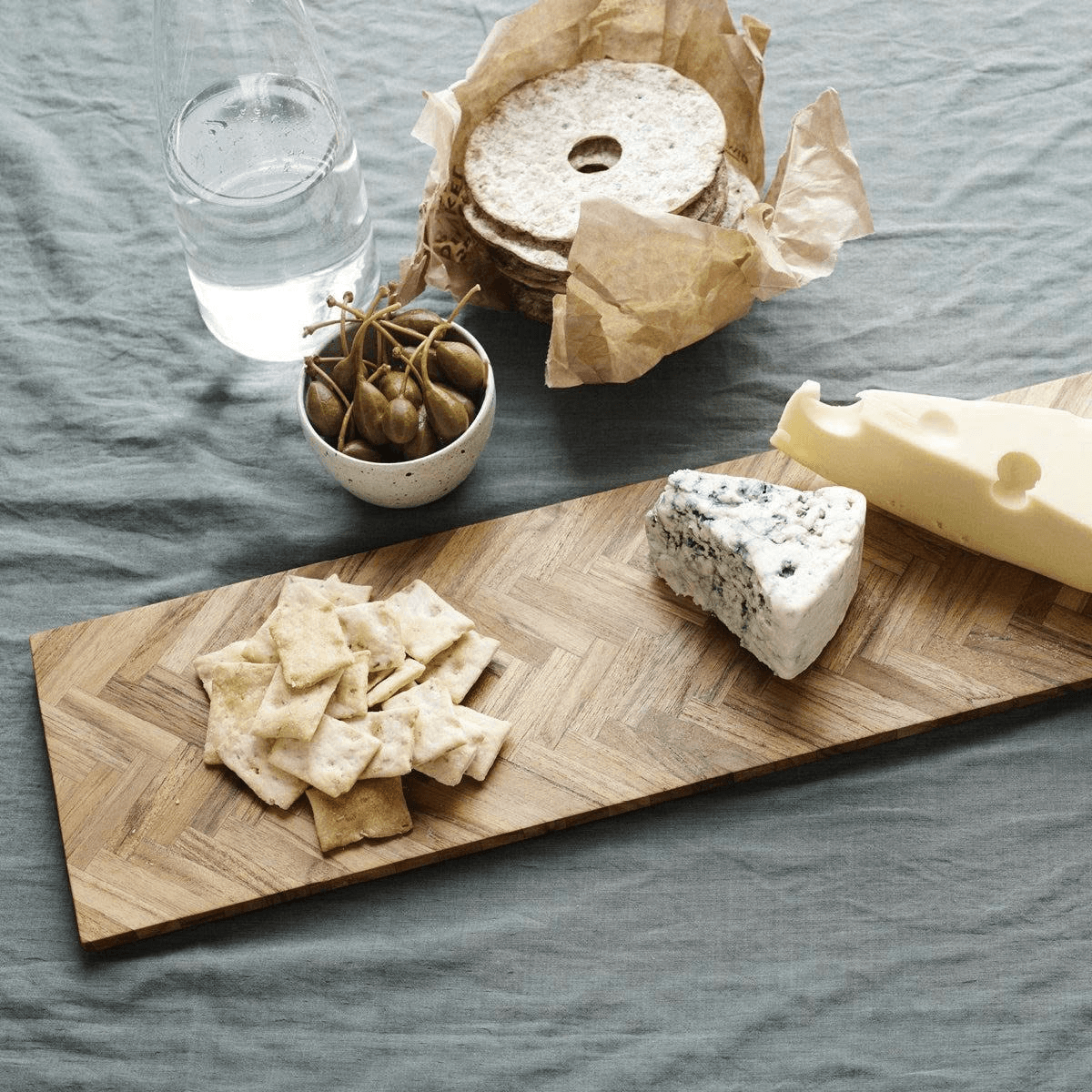 Teak herringbone serving board arranged with cheese and crackers